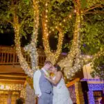 The newly weds standing in front of a tree wrapped with lighting effects