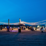 A group of people standing under a string of Bistro Lighting at dusk.