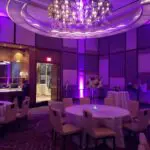 A room in Las Vegas with purple uplight rentals that create a mesmerizing ambiance, complete with stylish tables and chairs.