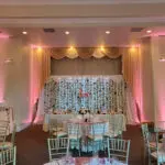 An indoor event setup with pink lights and white curtains