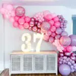 A pink and purple balloon arch decorated with marquee letter rental for a birthday party.