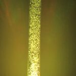 An acrylic LED bubble column water fountain in a dark room with a green light.