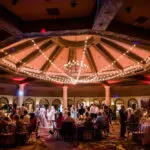 Lots of people standing under a huge chandelier-style light setup