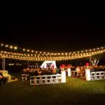 An outdoor event with white fences and hanging lights