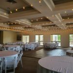 A large room adorned with string lights and furnished with white tables and chairs creates a beautifully lit atmosphere for events at Reflection Bay Las Vegas.