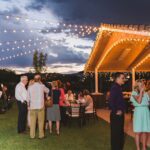 An enchanting wedding reception at dusk in a grassy area illuminated by string lights.