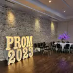 A stylishly decorated room with tables and chairs adorned with marquee letters spelling out "Prom 2020.