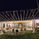 An enchanting wedding reception set up in a grassy area with elegant curtain light walls creating a romantic ambiance for the happy couple and their guests.